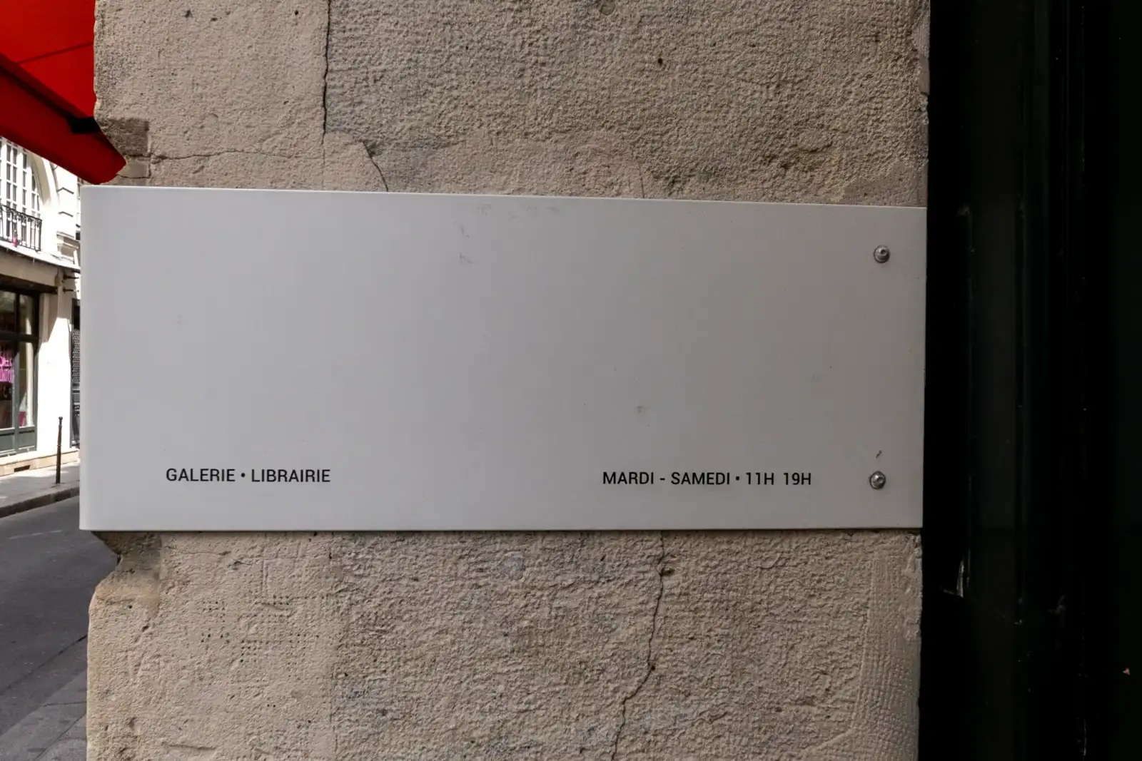 Un panneau blanc rectangulaire fixé sur un mur en pierre indique les horaires.
