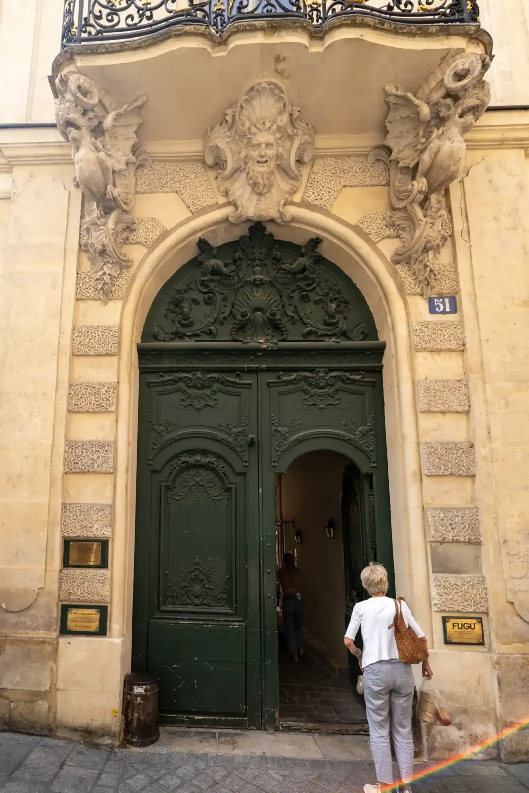 Une femme entre dans une grande porte cochère sculptée rue Saint Louis en l'Ile.