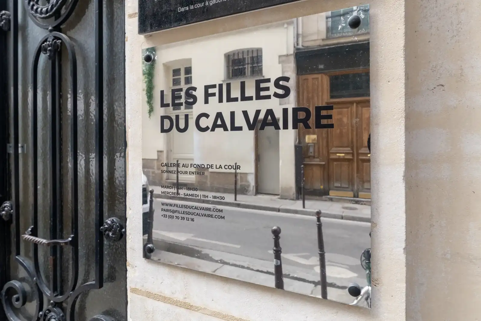 Plaque signalétique argentée de la galerie Les Filles du Calvaire fixée sur un mur.