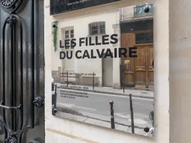 Plaque signalétique argentée de la galerie Les Filles du Calvaire fixée sur un mur.