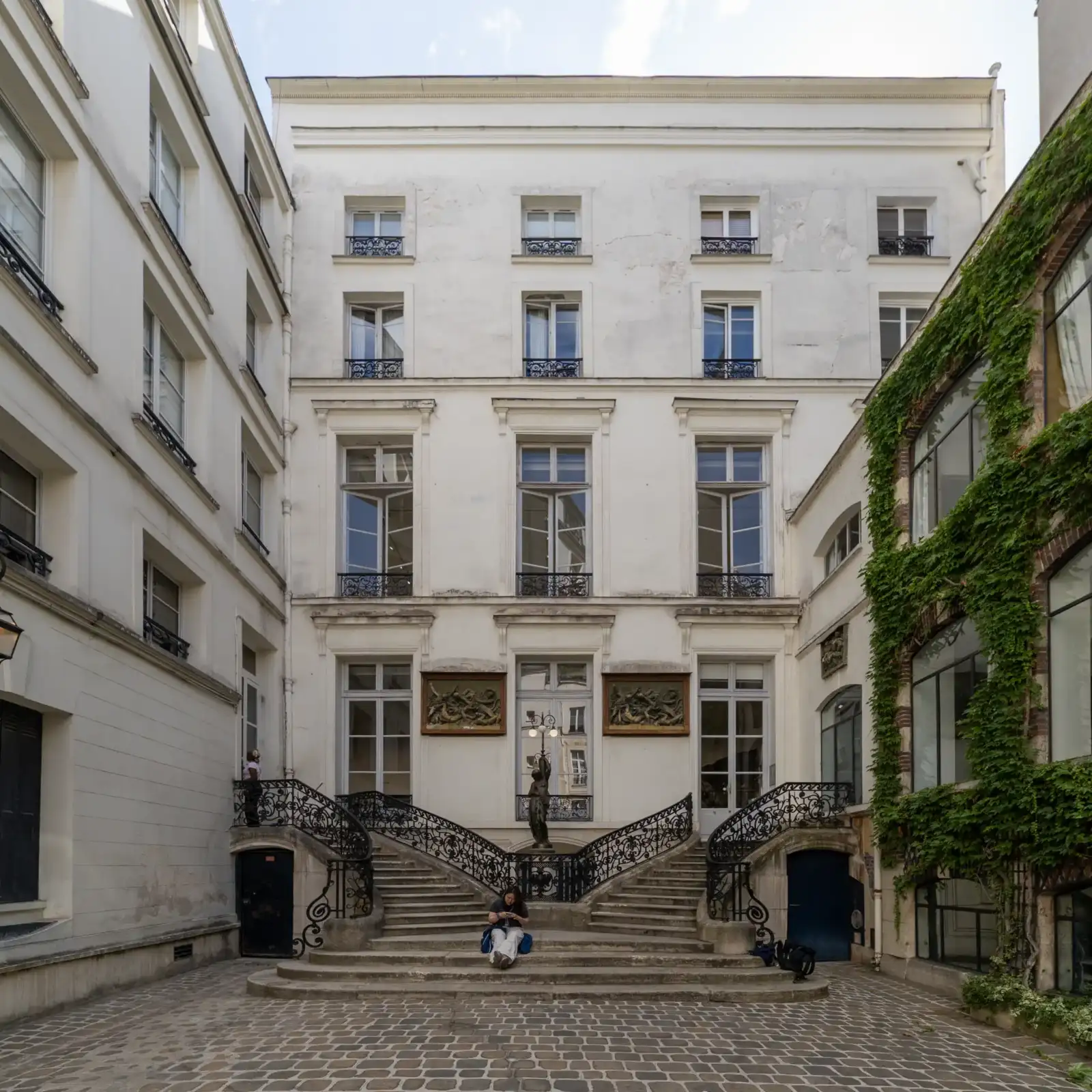 Une cour pavée avec un double escalier blanc menant à une galerie artistique.