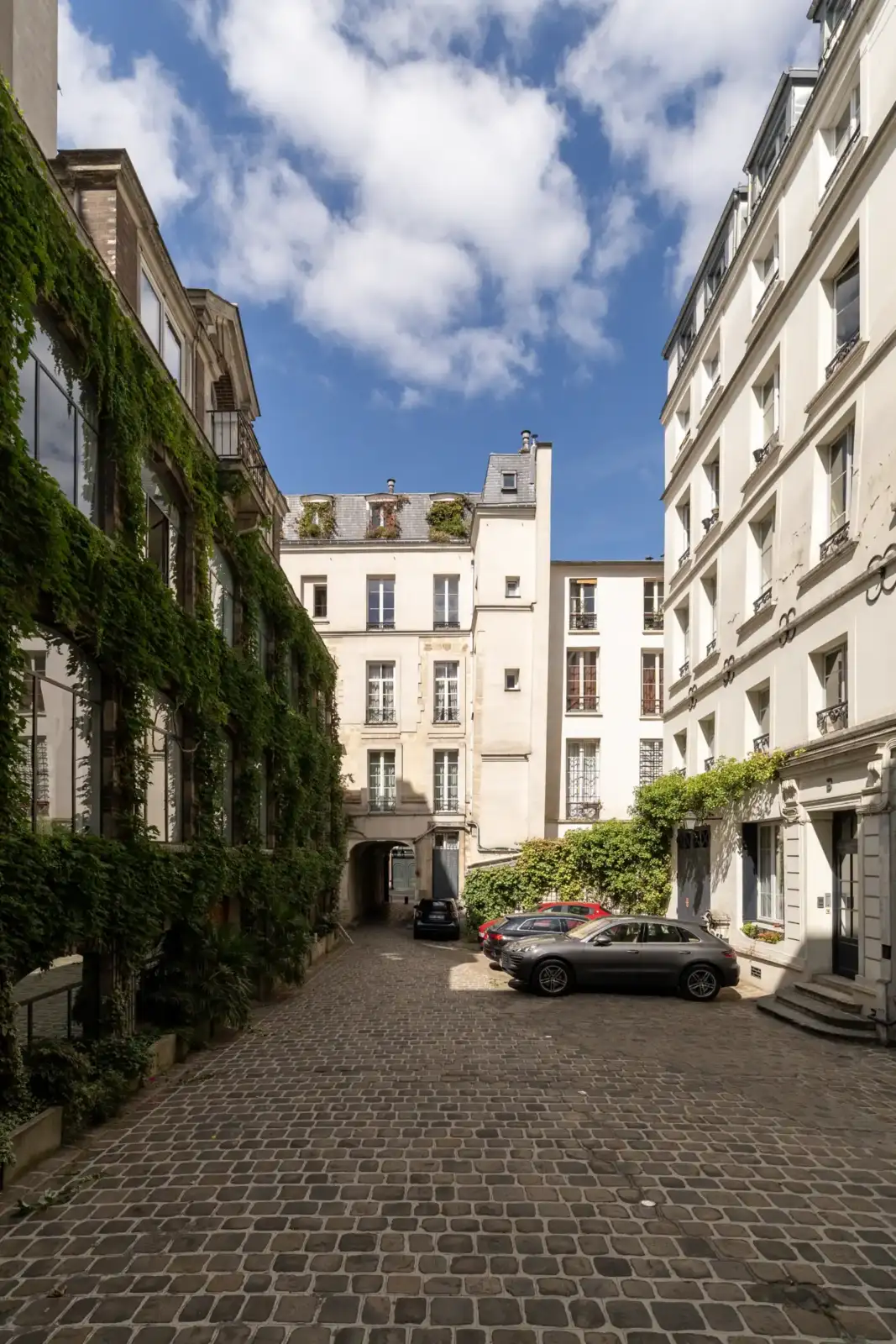 Une rue pavée bordée de bâtiments anciens et de verdure sous un ciel nuageux.