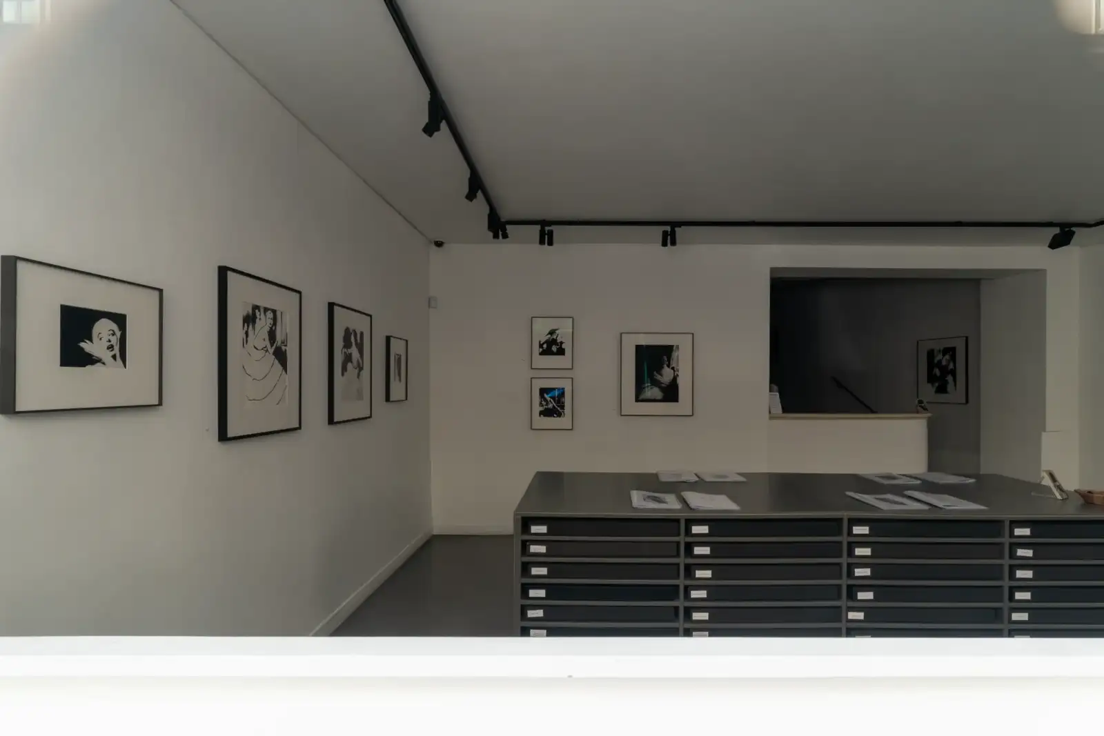 Vue intérieure d une galerie blanche avec des photographies encadrées et des meubles de rangement.