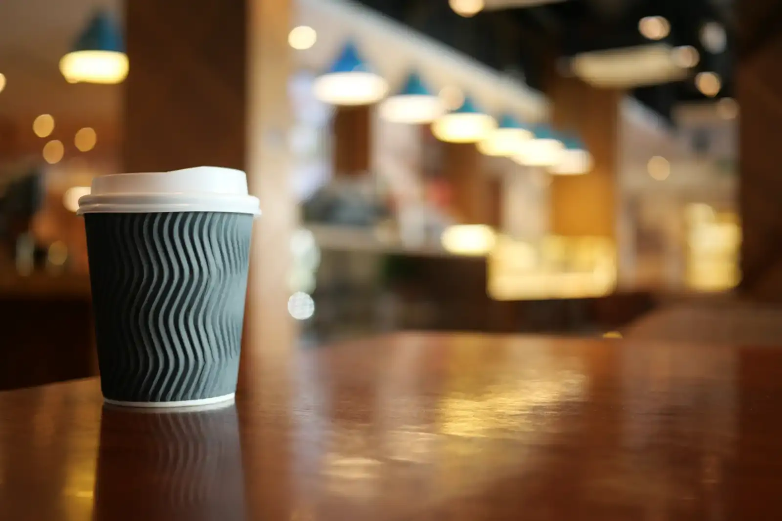 Un gobelet de café à emporter gris et blanc sur une table en bois.