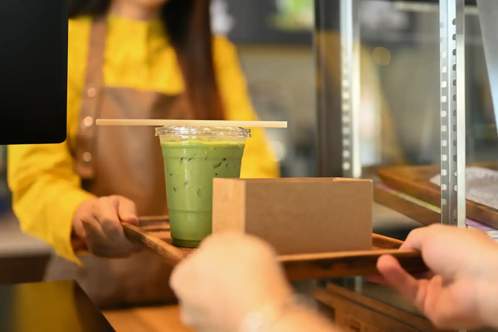 Une barista souriante tend un gobelet de matcha glacé sur un plateau en bois.