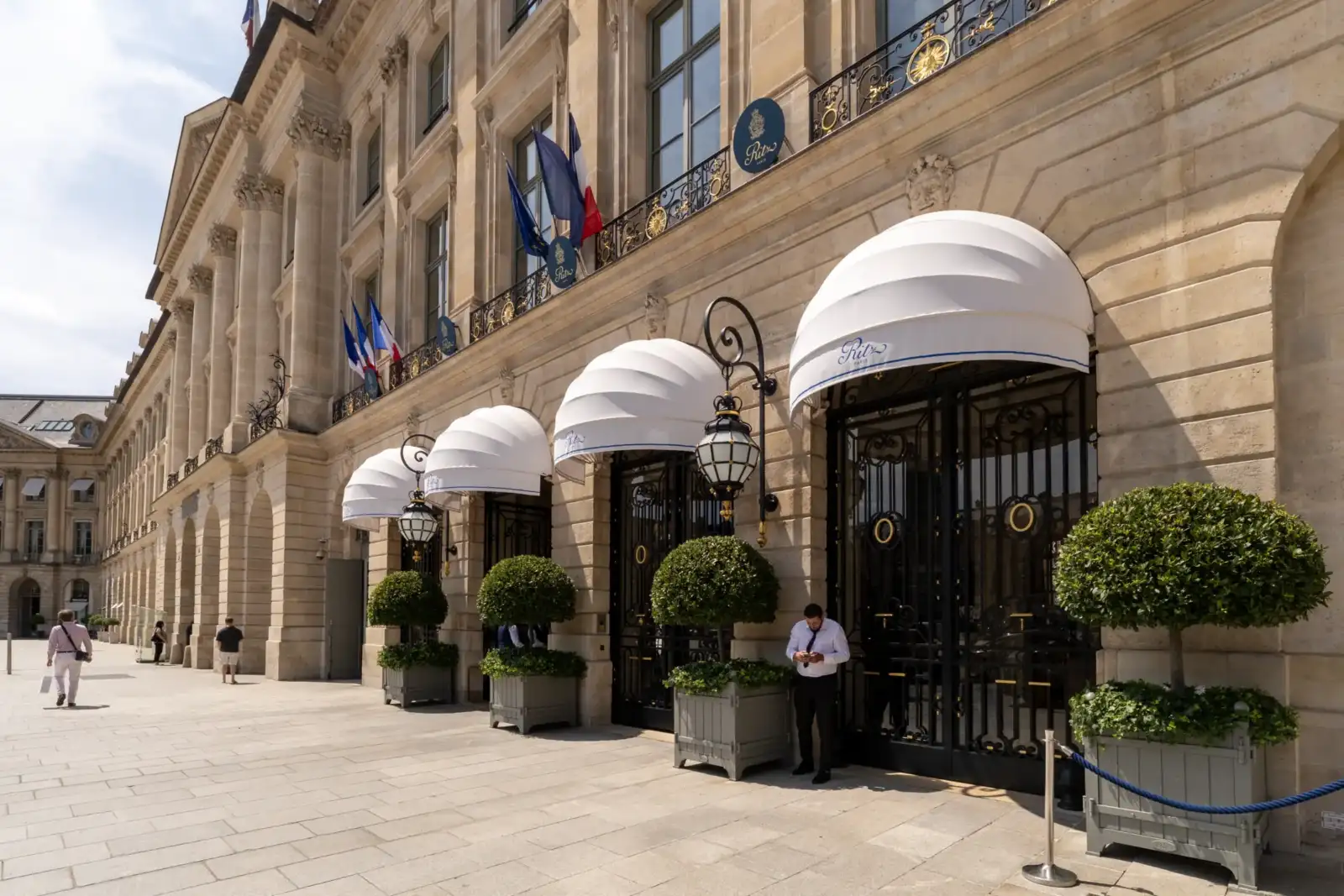 Façade élégante de l'hôtel Ritz à Paris, ornée de grands auvents blancs et d'arbustes taillés.