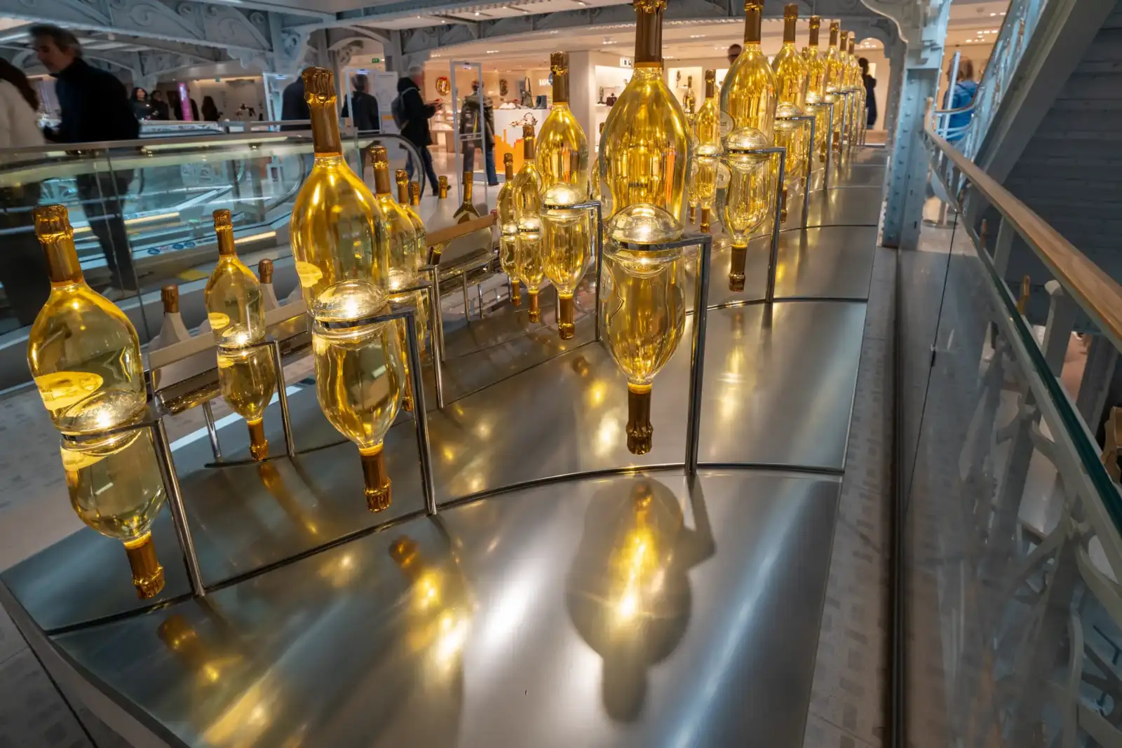 Des bouteilles dorées illuminées sont exposées sur un présentoir métallique au grand magasin Samaritaine.