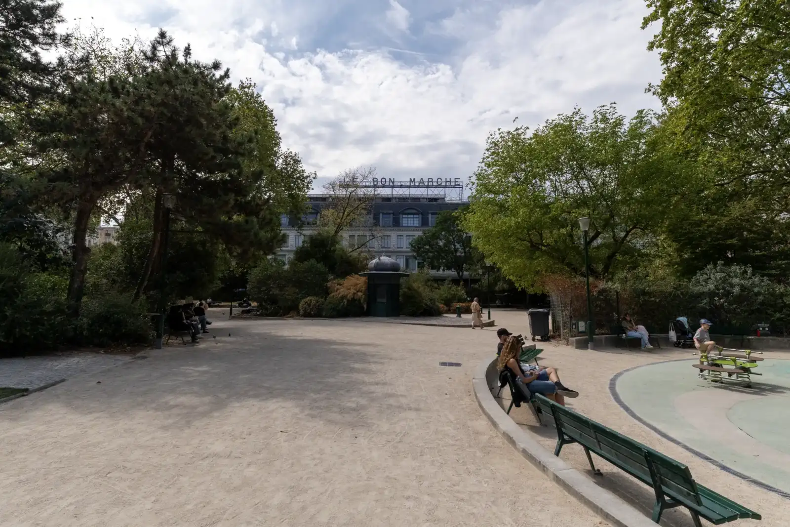 Des personnes se détendent dans un parc verdoyant face au grand magasin Le Bon Marché.