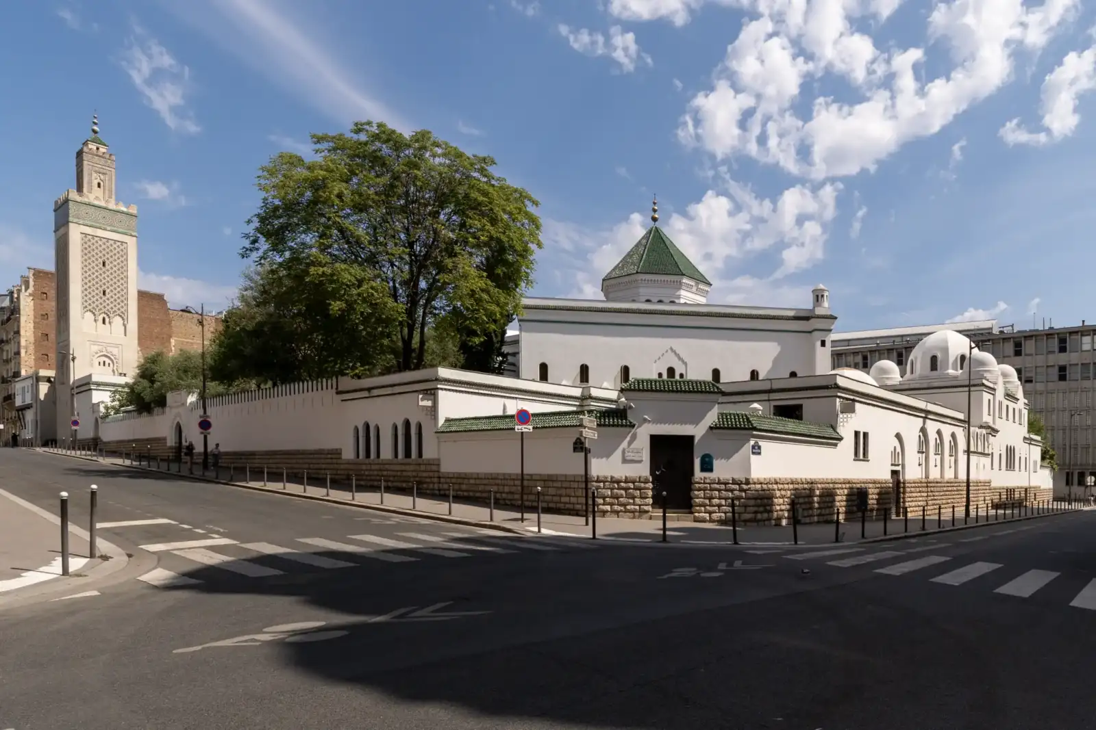 La grande mosquée blanche de Paris se dresse au coin d'une rue parisienne ensoleillée.