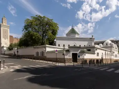 La grande mosquée blanche de Paris se dresse au coin d'une rue parisienne ensoleillée.