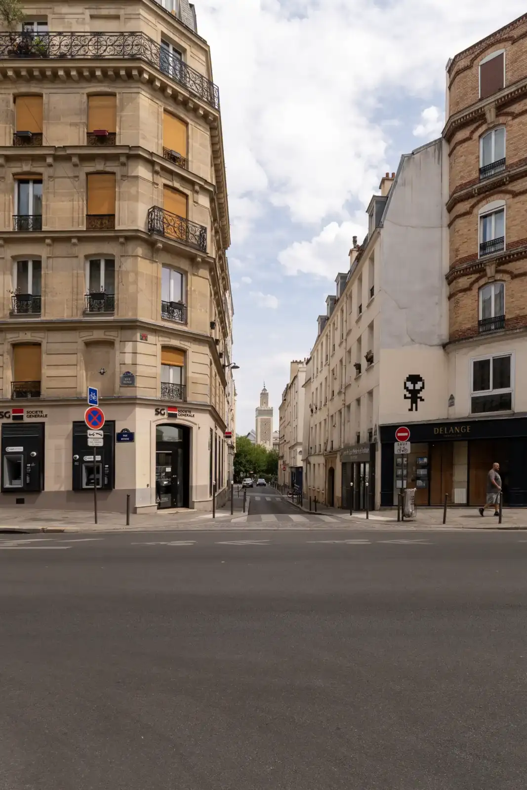 Une rue parisienne encadrée par des immeubles haussmanniens avec le minaret de la grande mosquée en arrière-plan.