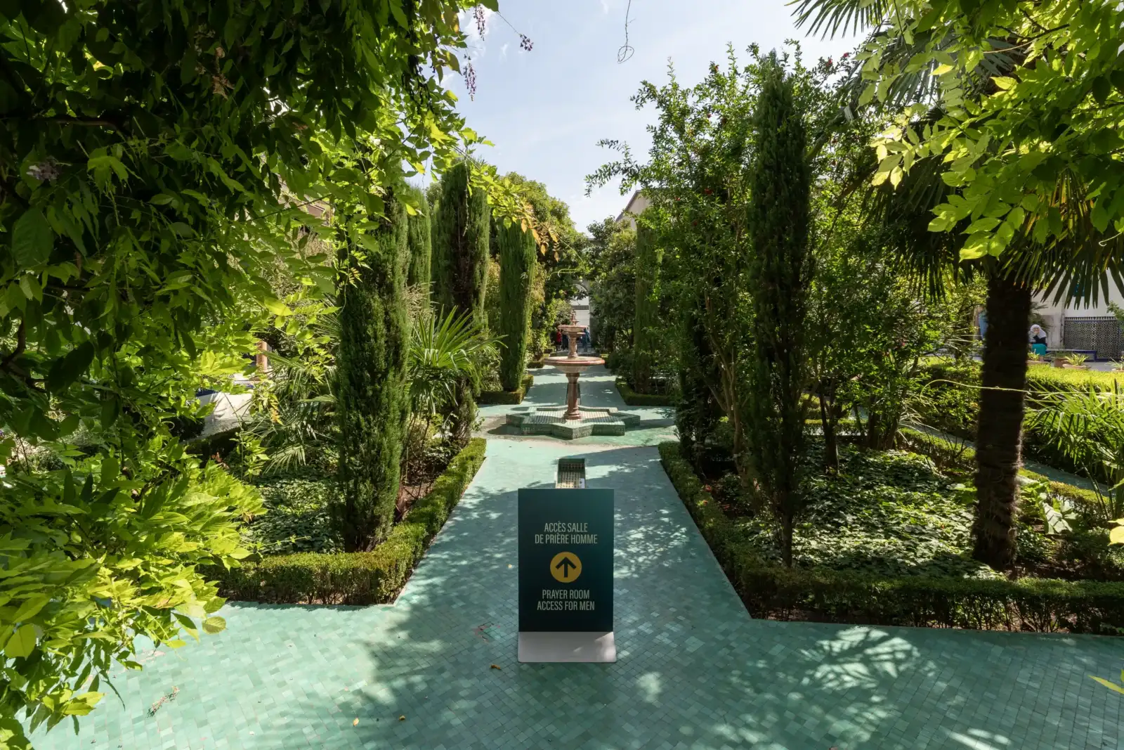 Un panneau indicateur vert guide vers la salle de prière masculine dans le jardin luxuriant.