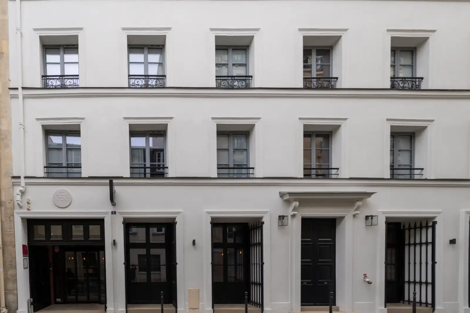 Façade blanche élégante d'un hôtel parisien avec des fenêtres grises et portes noires.