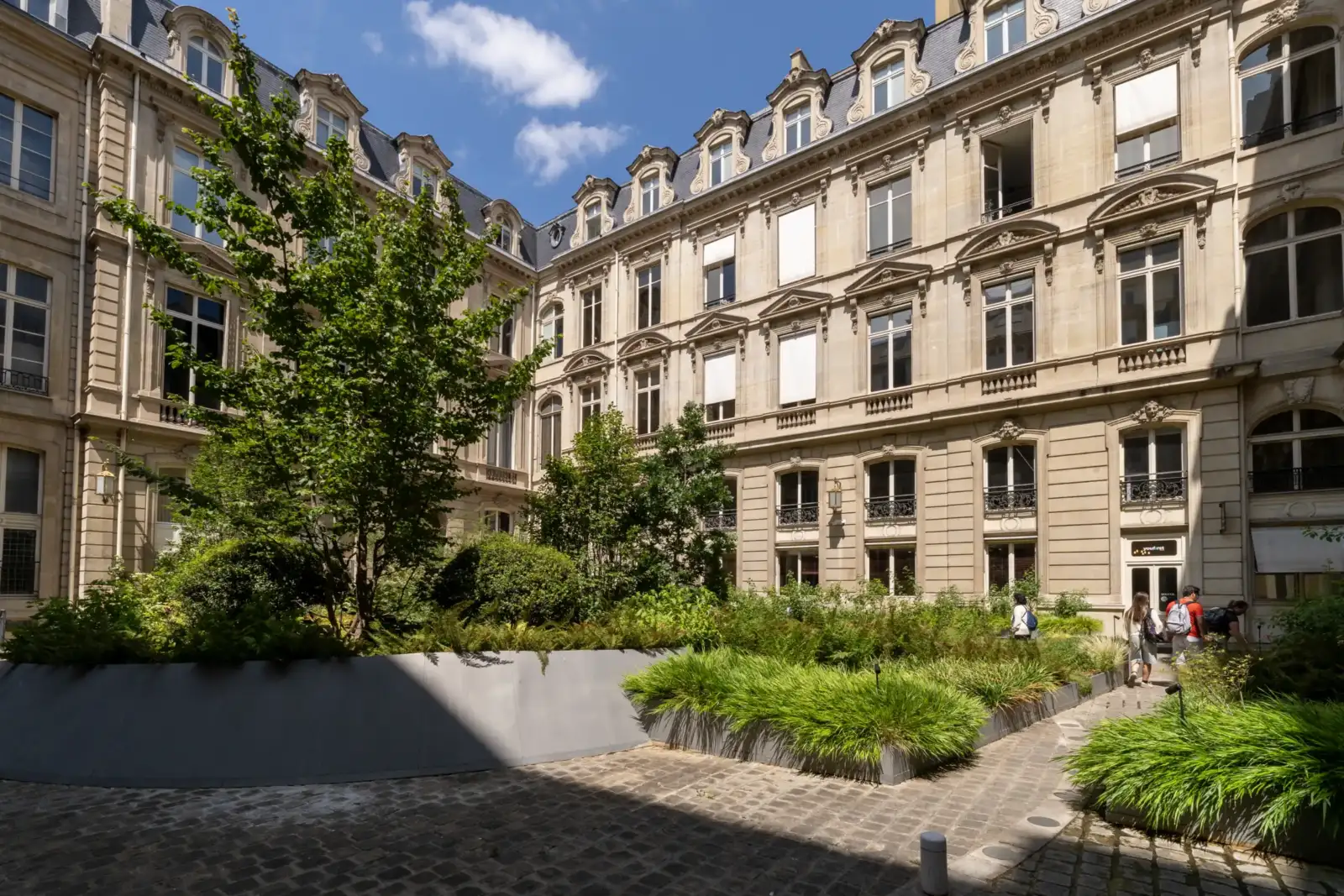 Une cour intérieure pavée avec un jardin verdoyant bordée par des bâtiments classiques parisiens.