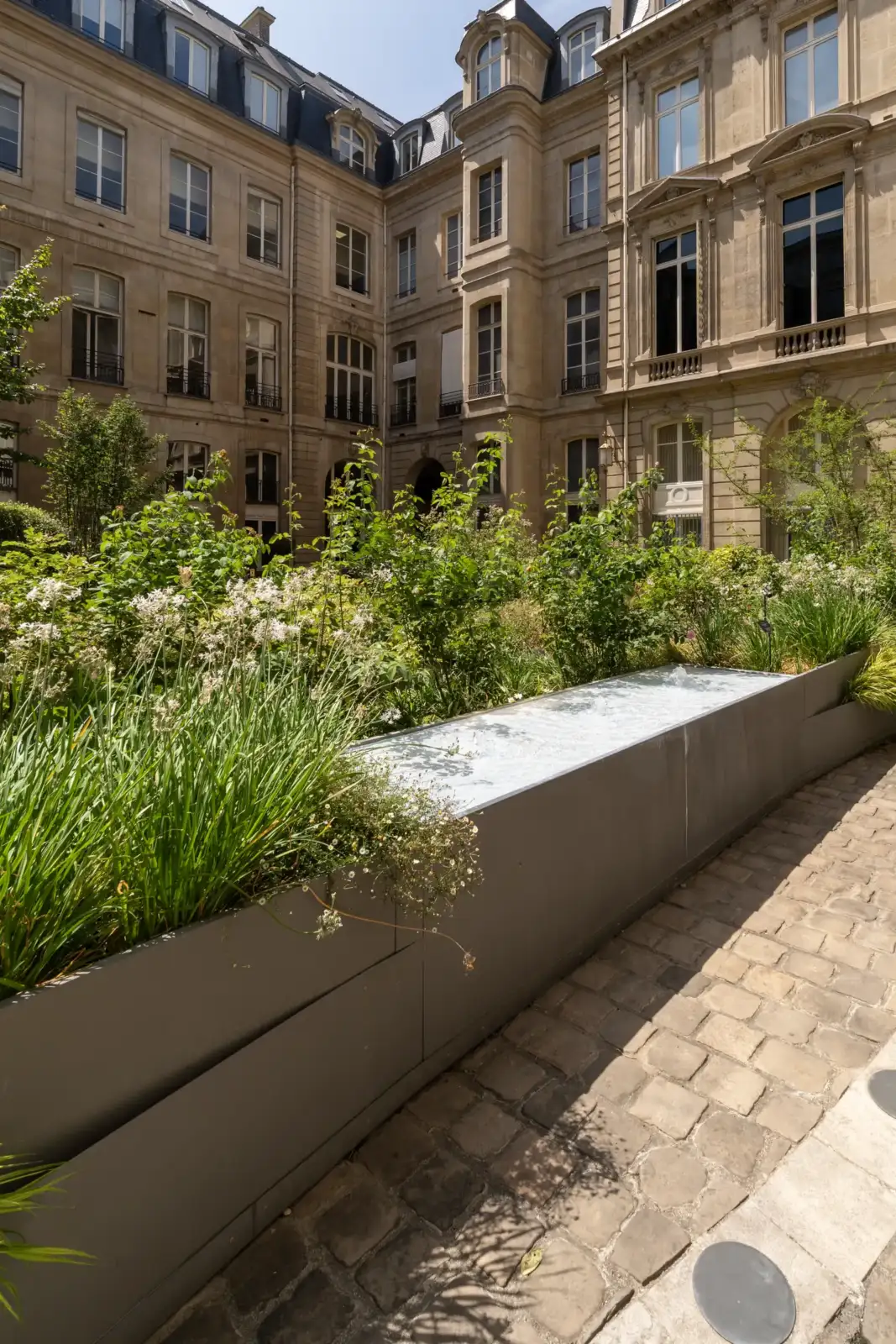 Une cour pavée de l'hôtel Baudard Saint-James ornée d'un long bassin entouré de verdure.