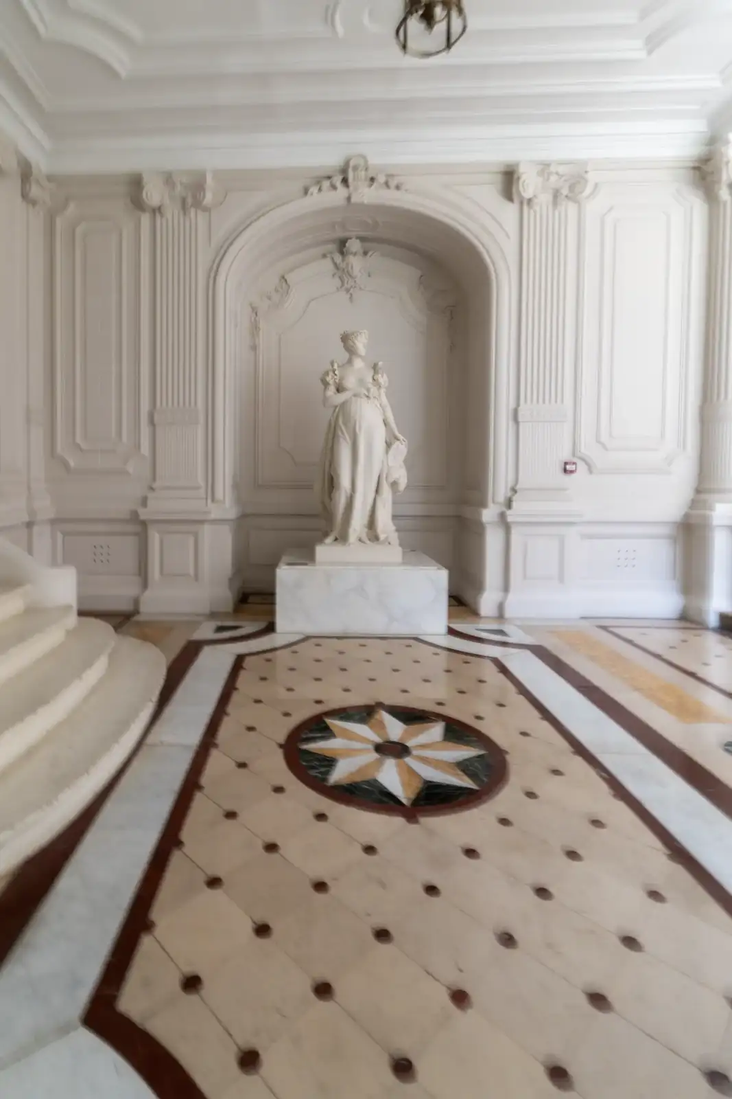 Une statue féminine blanche se dresse au fond d un hall classique orné.
