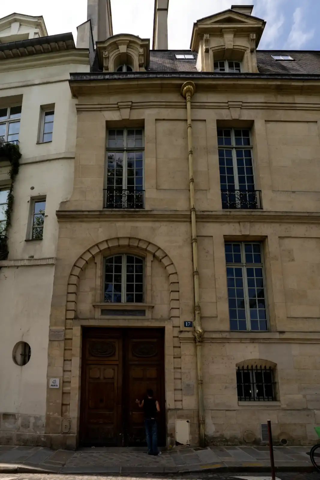 Une personne est debout devant la grande porte en bois de cet hôtel particulier parisien.