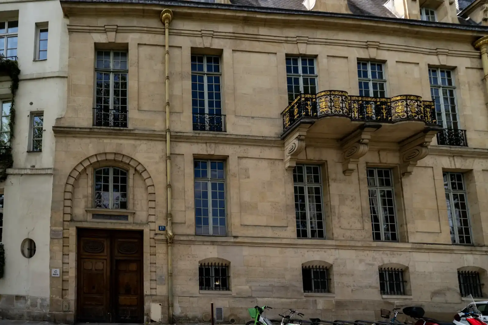 Façade classique en pierre claire avec de grandes fenêtres et un balcon en fer forgé doré.
