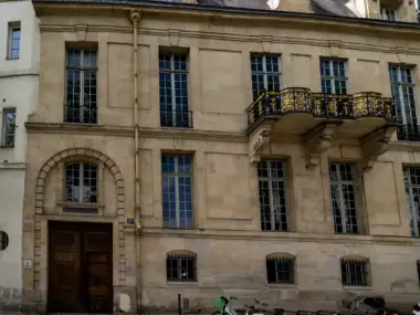 Façade classique en pierre claire avec de grandes fenêtres et un balcon en fer forgé doré.