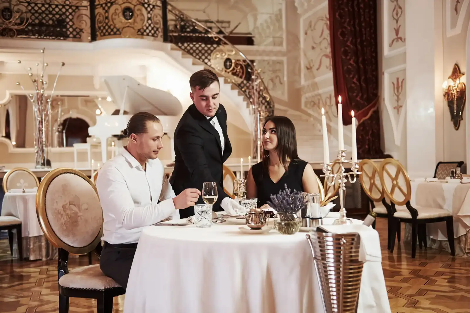 Un serveur sert un couple élégant dans le salon somptueux d un palace parisien.