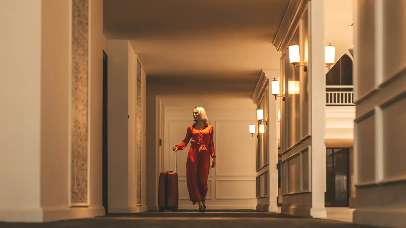 Une femme blonde en combinaison rouge marche dans un couloir d hôtel luxueux.