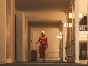 Une femme blonde en combinaison rouge marche dans un couloir d hôtel luxueux.