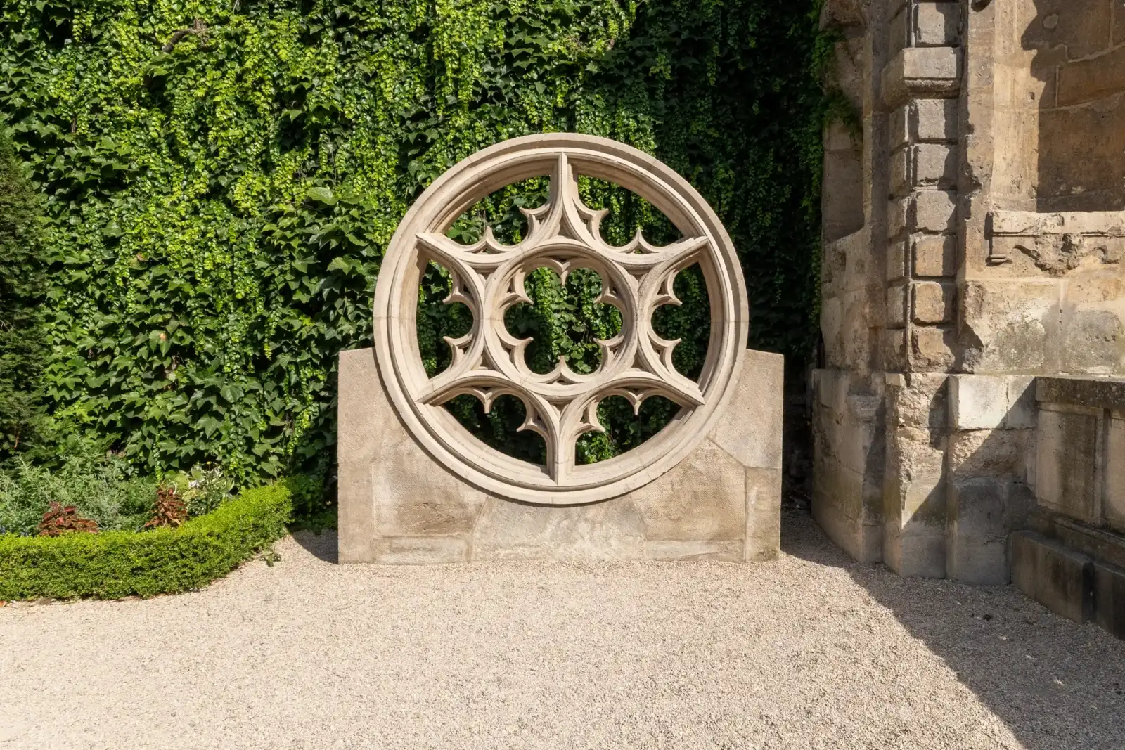 Une rosace en pierre sculptée est exposée devant un mur de verdure luxuriante.