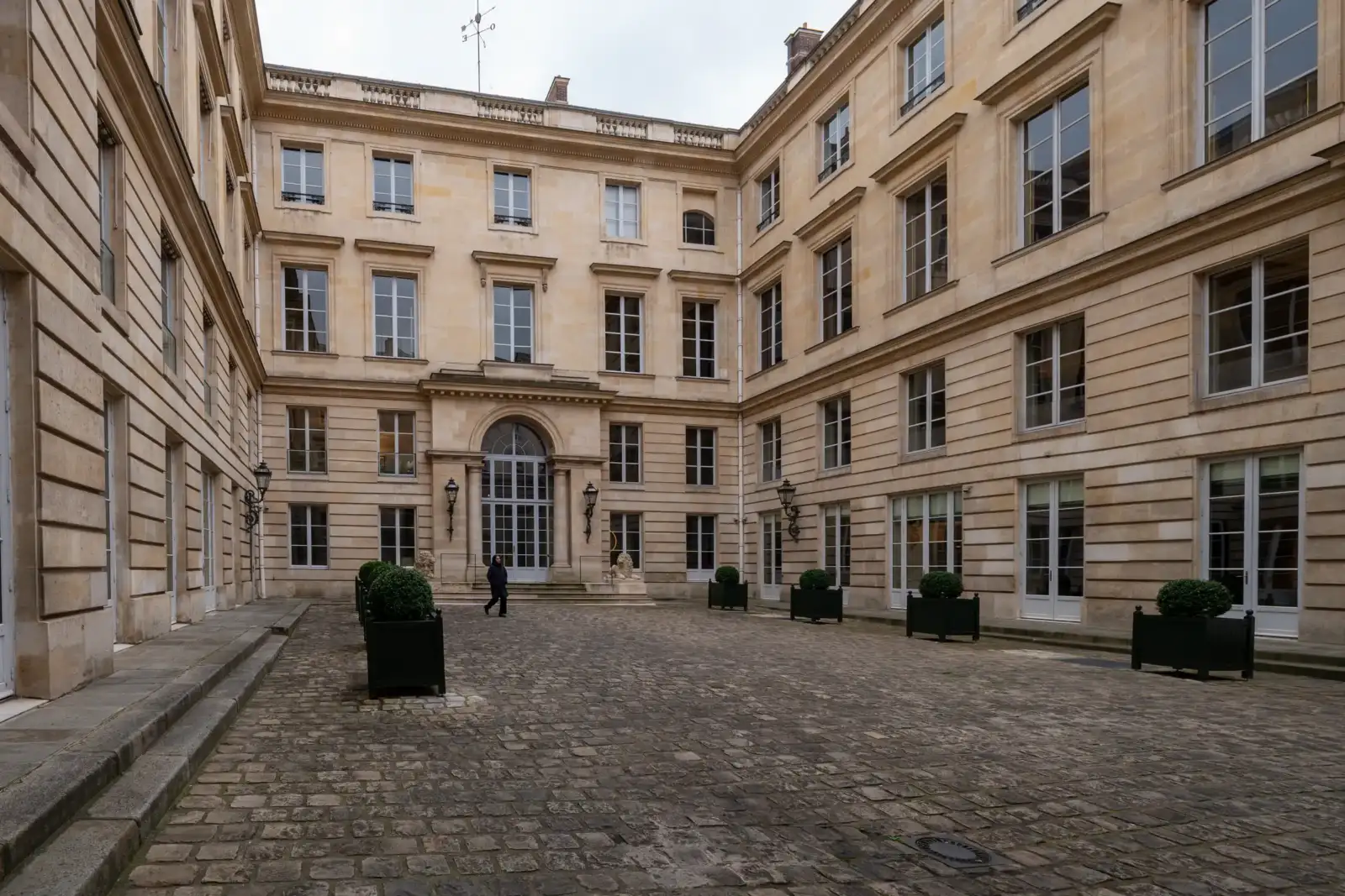 Une personne marche dans la cour pavée de l'élégant hôtel Talleyrand à Paris.