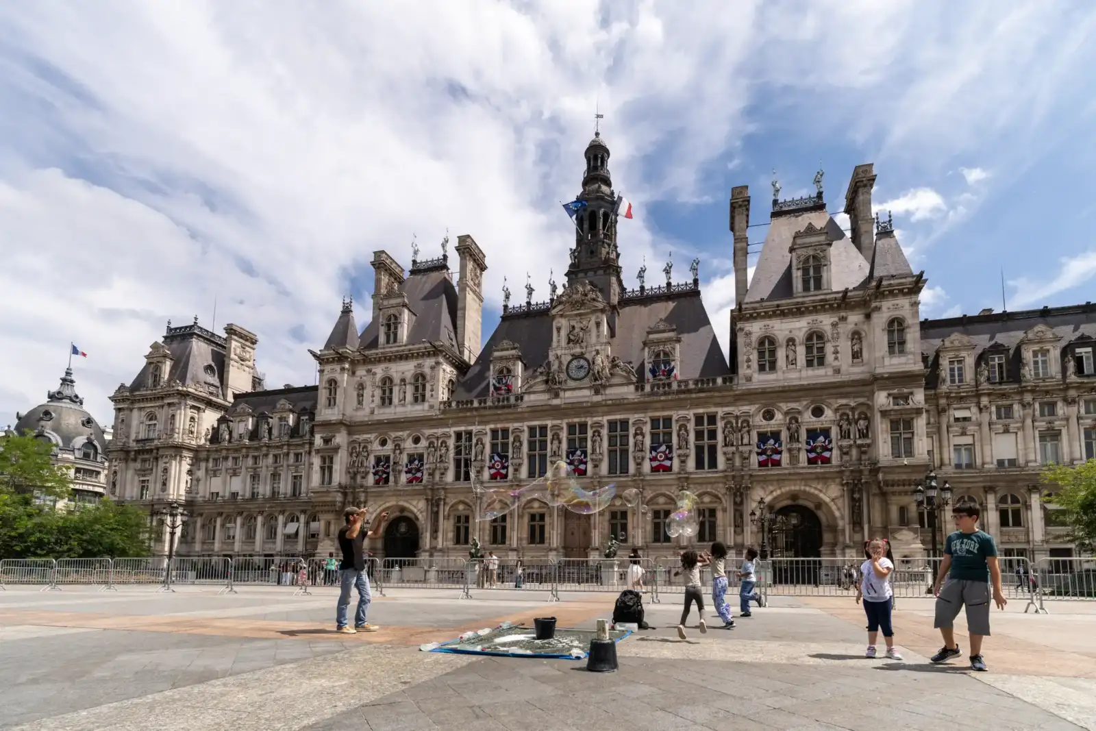 Des enfants jouent avec des bulles géantes devant la majestueuse façade de l'Hôtel de Ville de Paris.