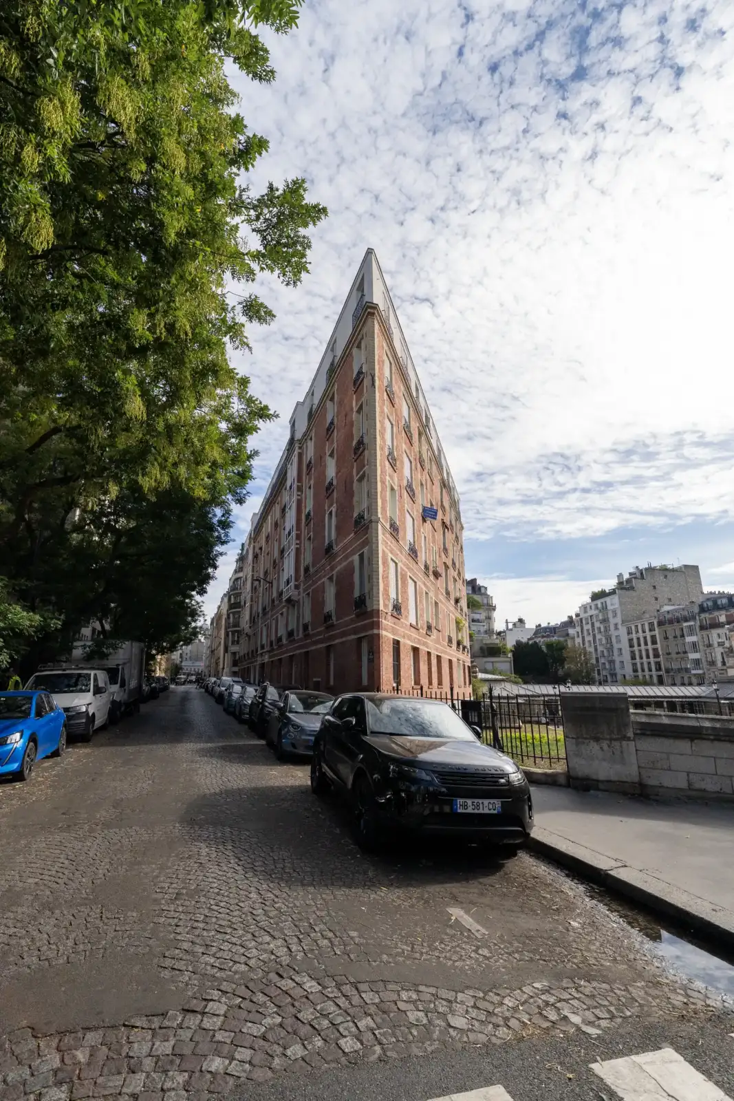 Vue en contre-plongée d'un immeuble triangulaire très étroit bordant une rue pavée parisienne.