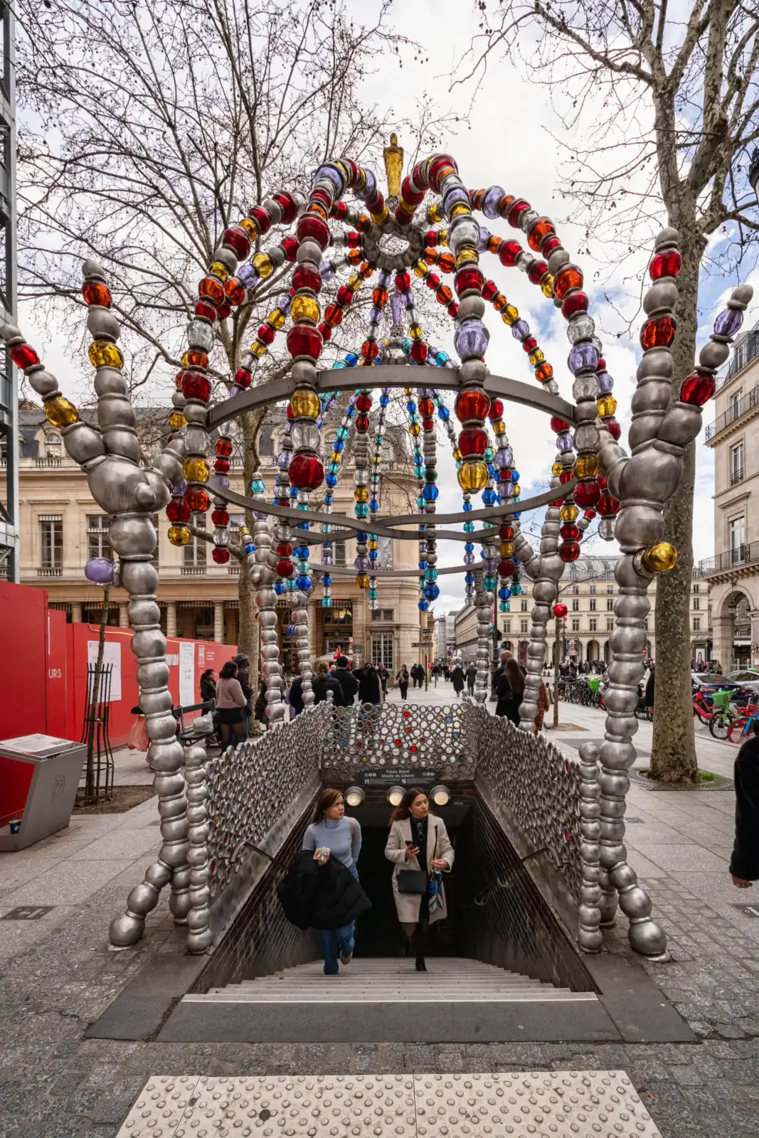 L'entrée colorée du métro parisien Kiosque des Noctambules avec des passants montant les escaliers.