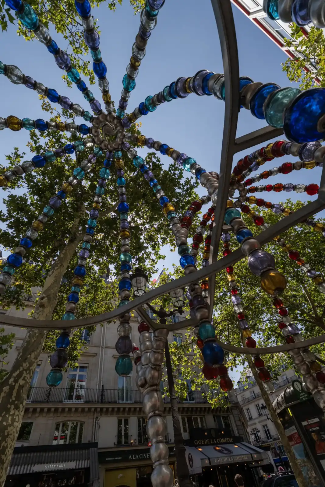 Une installation artistique de perles en verre multicolores suspendues sous un ciel bleu.