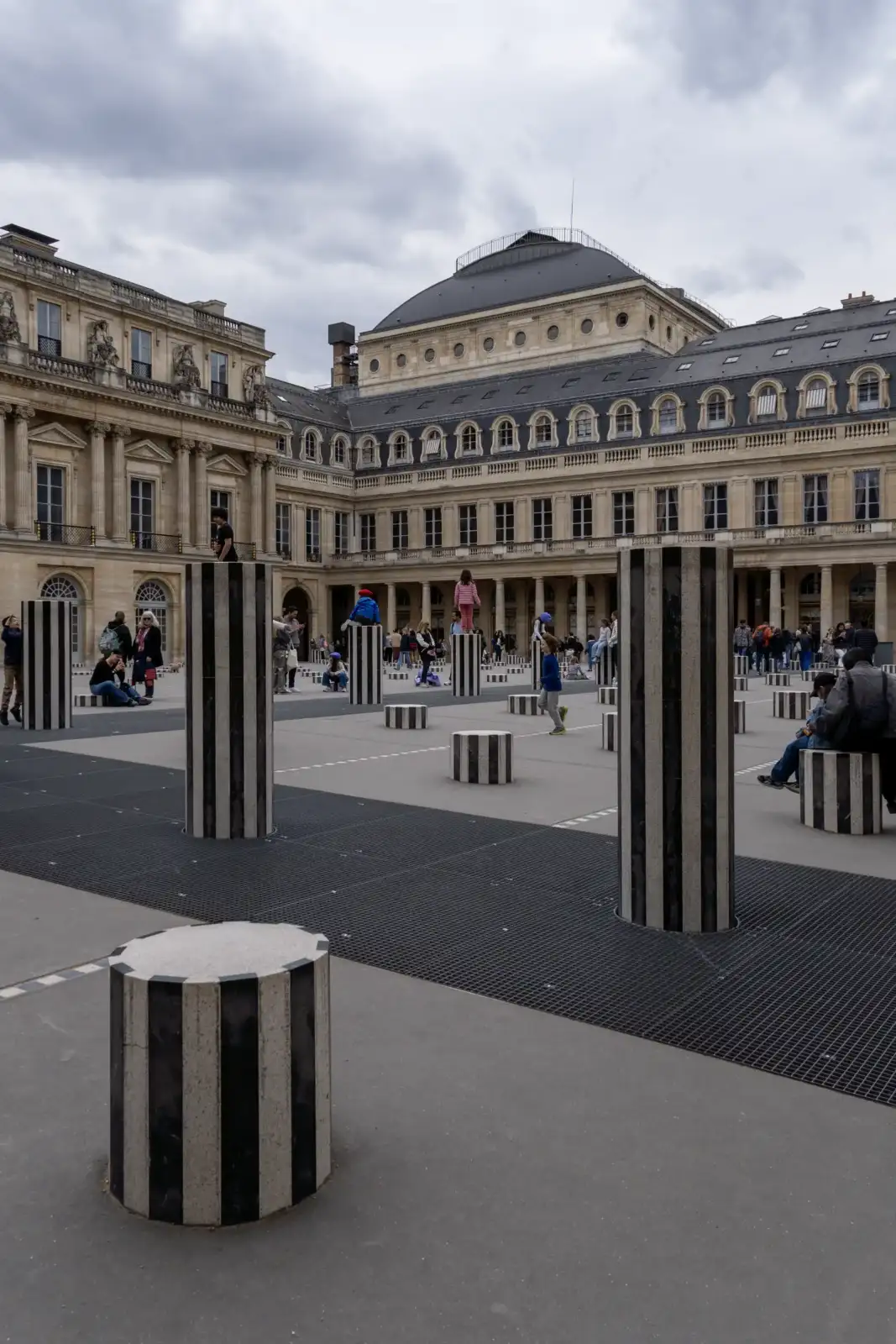 Des personnes se promènent parmi les colonnes rayées de Buren dans la cour parisienne.