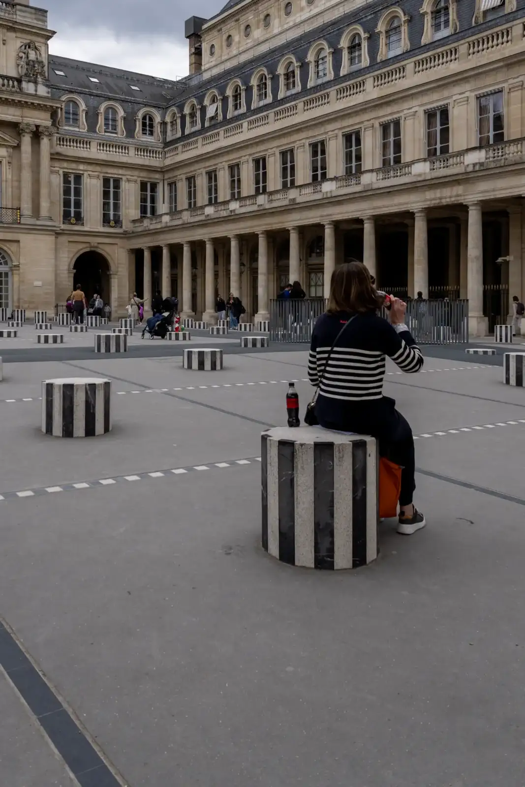 Une femme assise sur une colonne de Buren rayée dans la cour du Palais-Royal.