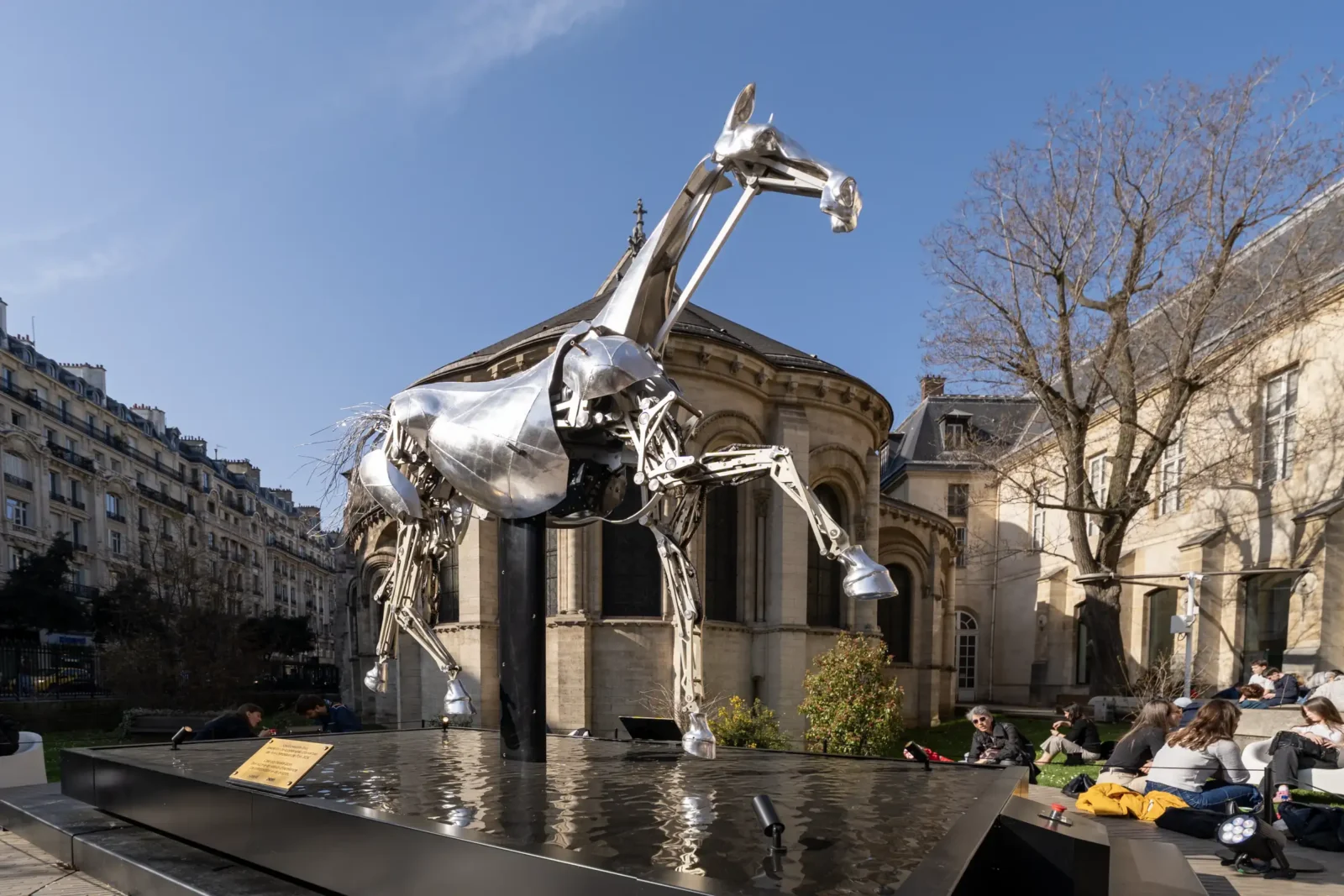 Une sculpture métallique de cheval trône au centre d'un bassin dans un parc parisien.