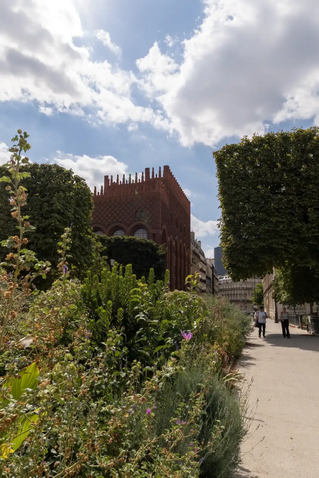 Vue extérieure d un bâtiment en brique rouge entouré de verdure et de passants.