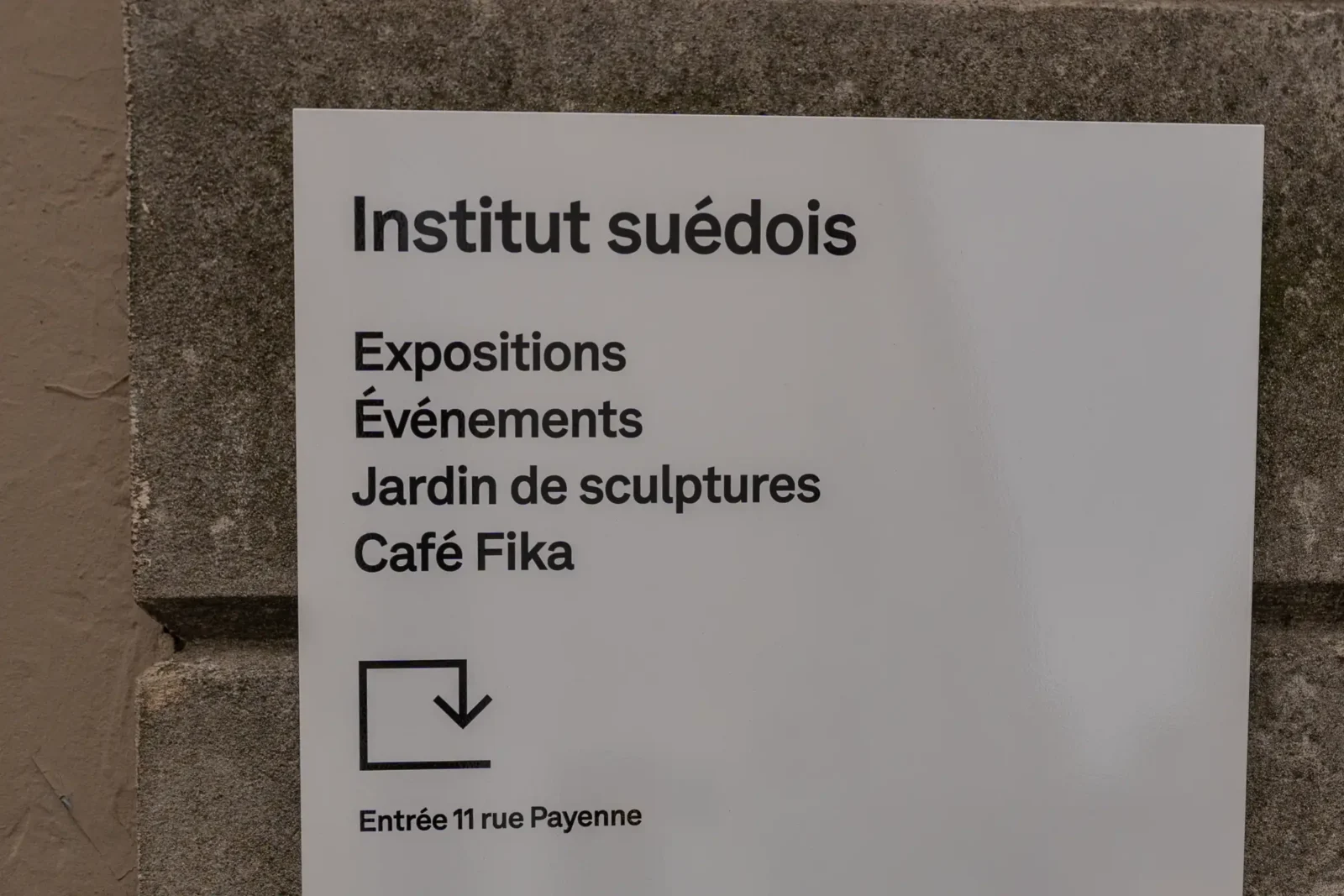 Panneau signalétique blanc indiquant l'Institut suédois fixé sur un mur en pierre grise.