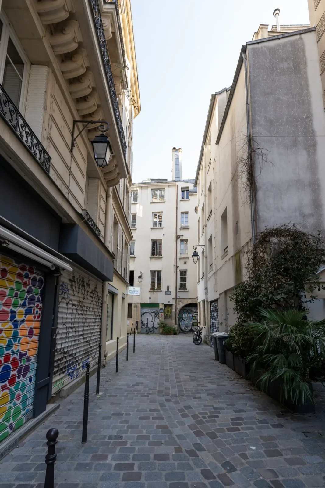 Une ruelle pavée étroite bordée d'immeubles parisiens anciens avec des volets et graffitis colorés.