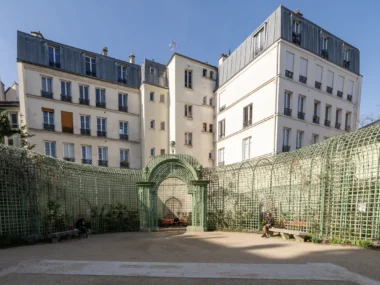 Une structure en treillage vert entoure une cour parisienne sous un ciel bleu clair.
