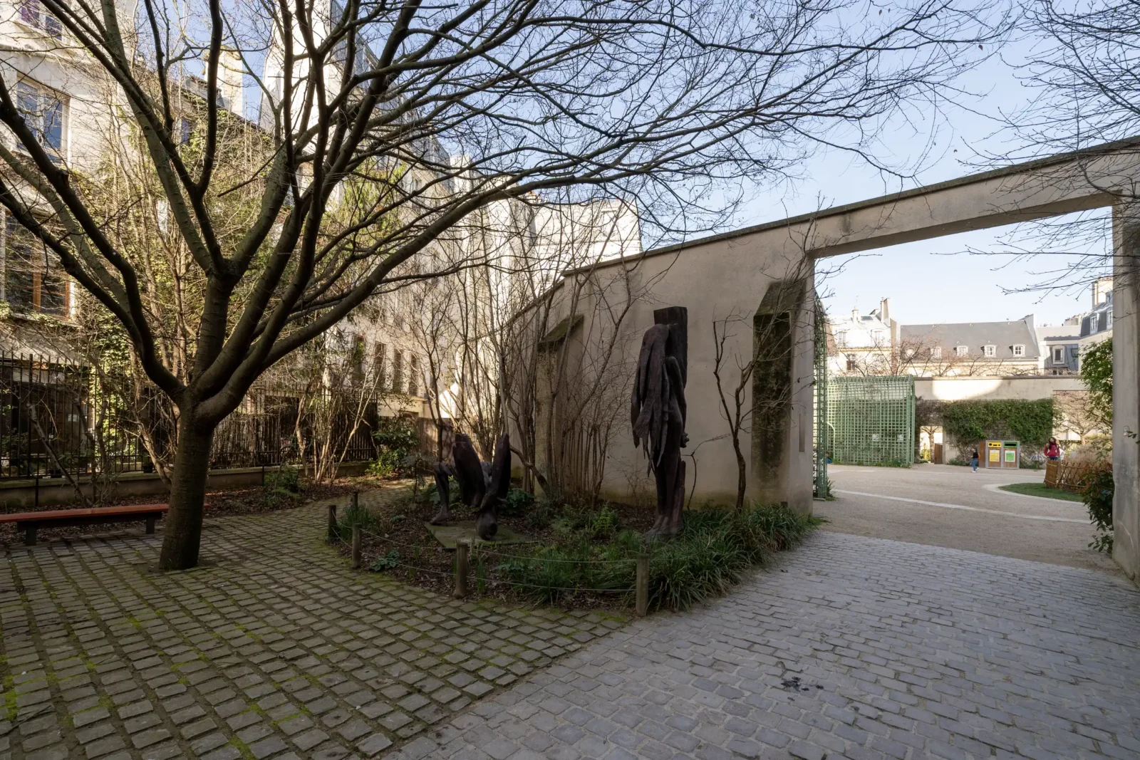 Sculptures se dressent dans le calme jardin Anne Frank sous un grand arbre dénudé.