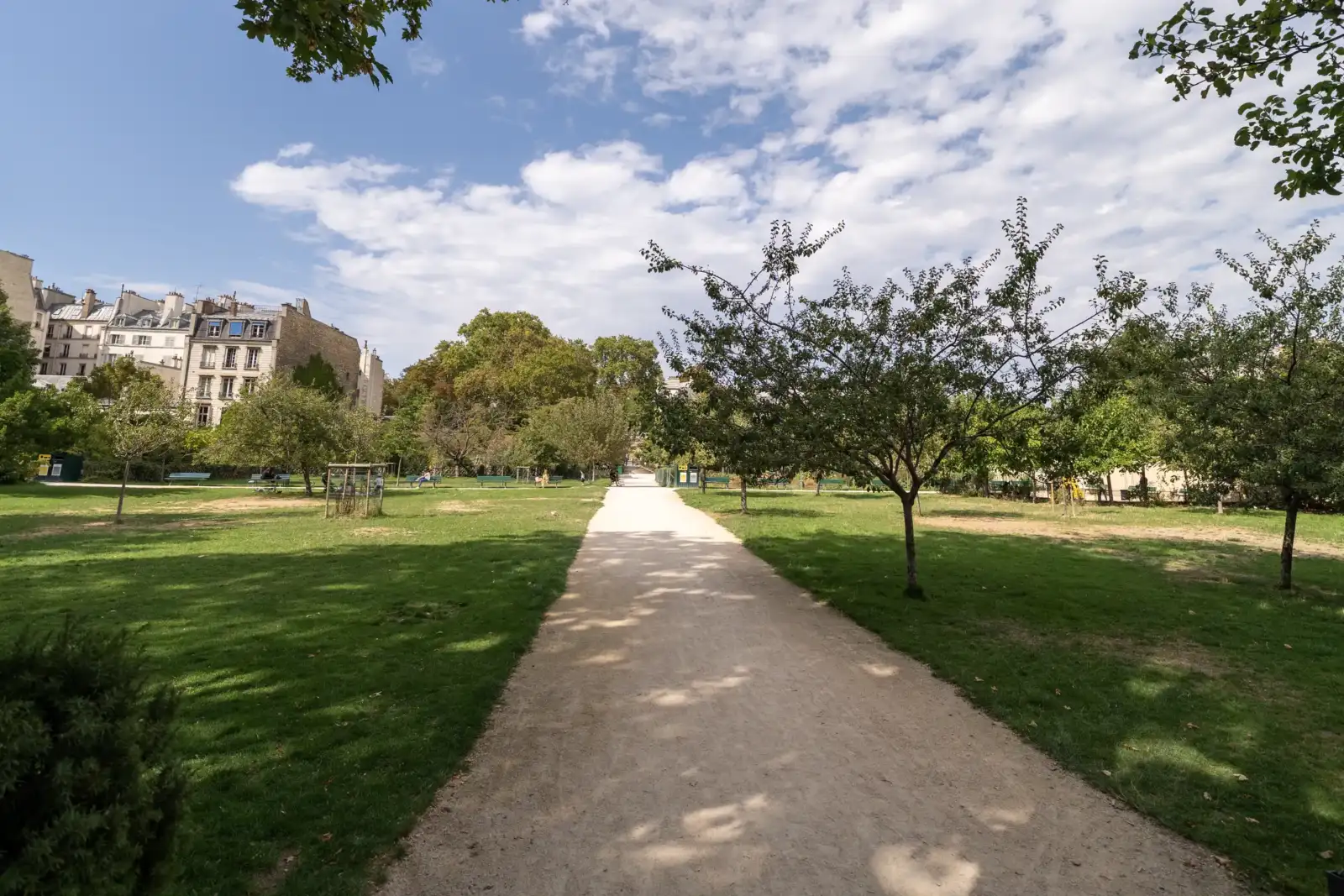 Allée de gravier bordée de pelouses et d'arbres sous un ciel nuageux.