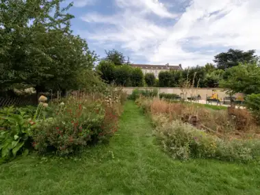 Une allée herbeuse sépare des massifs fleuris sous un ciel nuageux au jardin parisien.