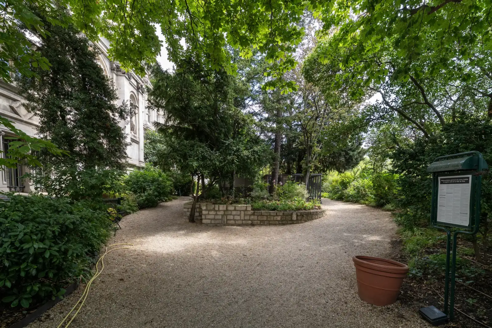 Une allée gravillonnée serpente au milieu de la verdure ombragée du jardin parisien.