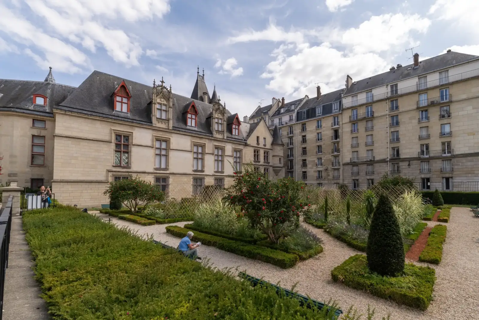 Un paisible jardin historique entoure de bâtiments parisiens anciens sous un ciel nuageux.