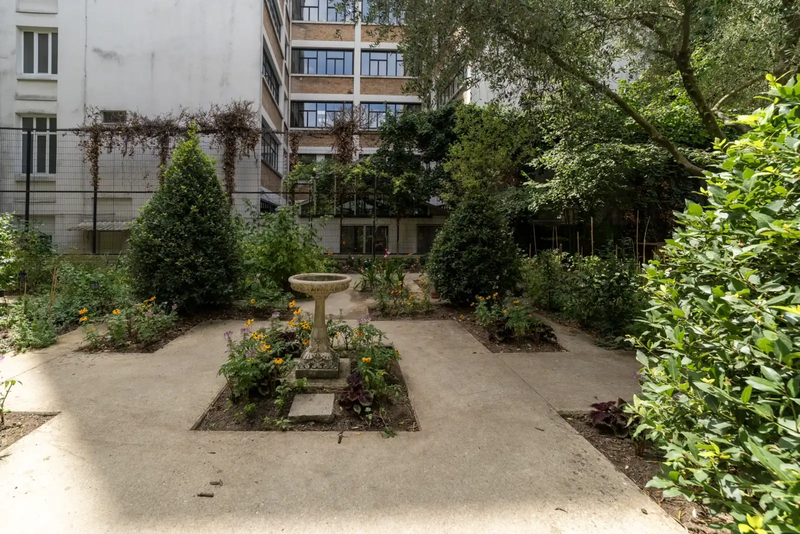 Un jardin partagé arboré et fleuri au milieu de hauts bâtiments parisiens.