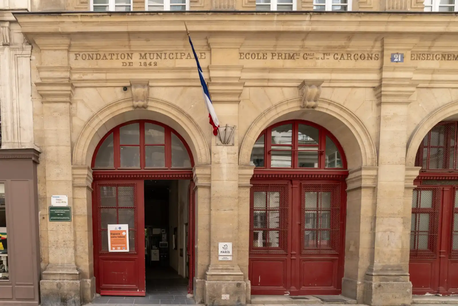 Façade classique en pierre avec des portes rouges en arc et inscriptions anciennes.