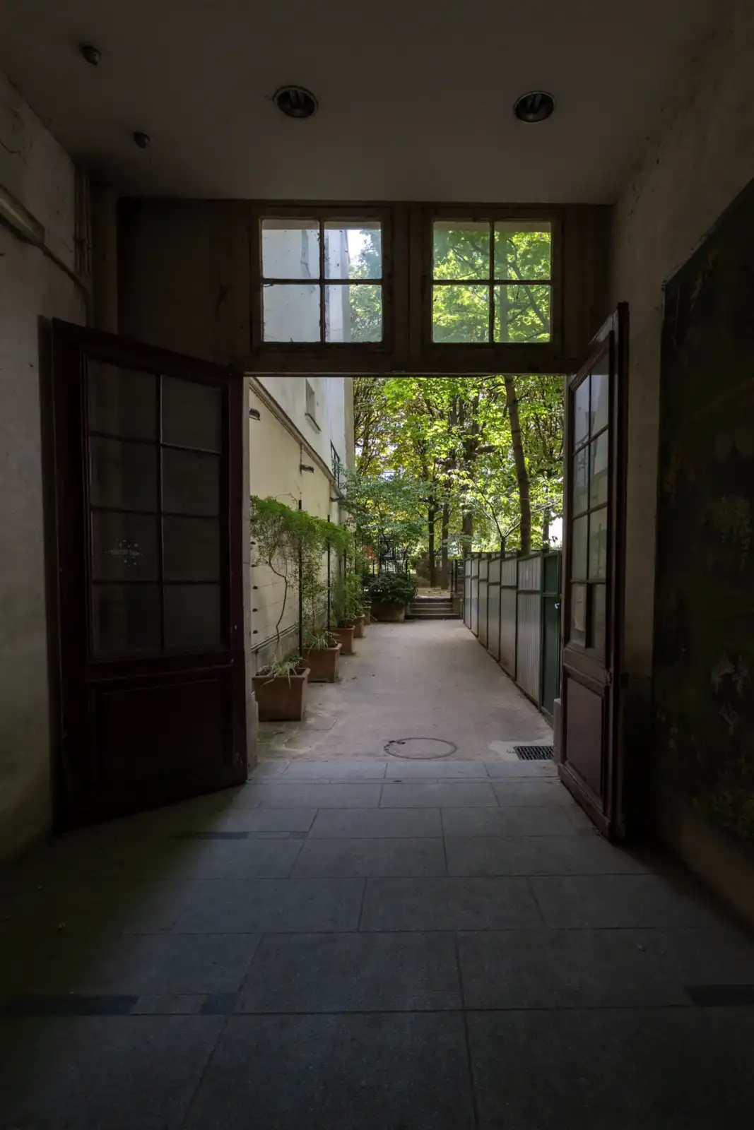 Vue depuis un hall sombre sur un jardin verdoyant et ensoleillé à Paris.
