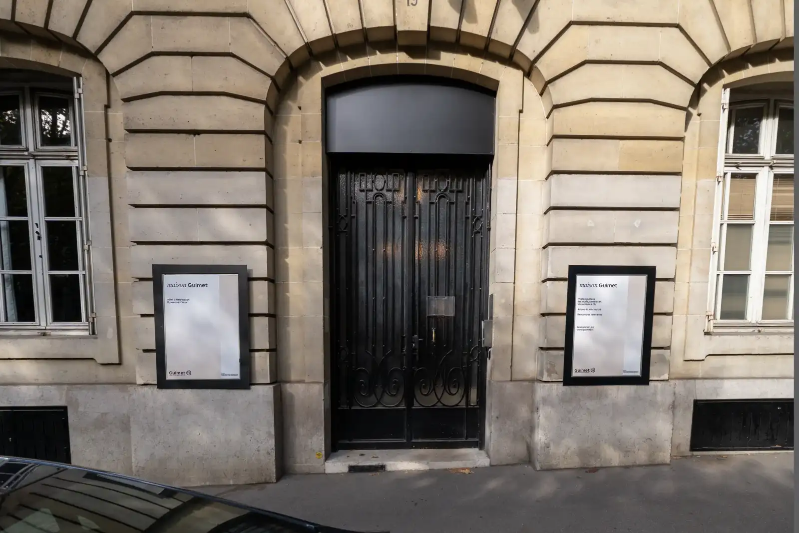 Façade en pierre beige avec une porte métallique noire et deux panneaux informatifs.