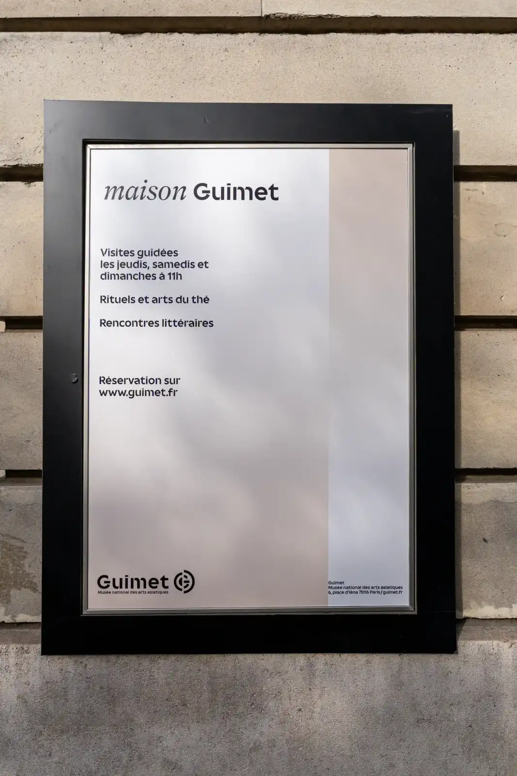 Un panneau d'affichage noir fixé sur un mur en pierre indique Maison Guimet.