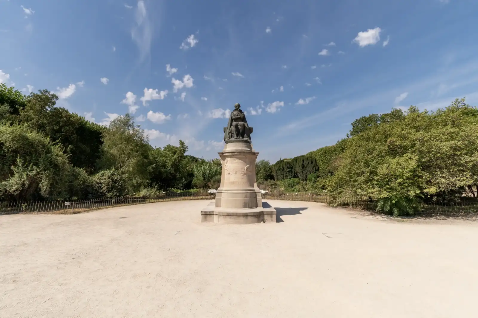 Une statue en bronze sur un socle de pierre au milieu d un jardin ensoleillé.